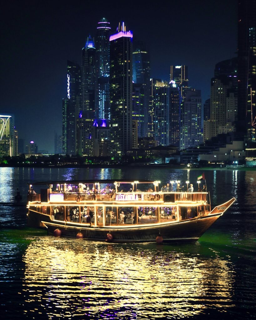 A traditional dhow boat illuminated against the stunning night skyline of Dubai Marina.