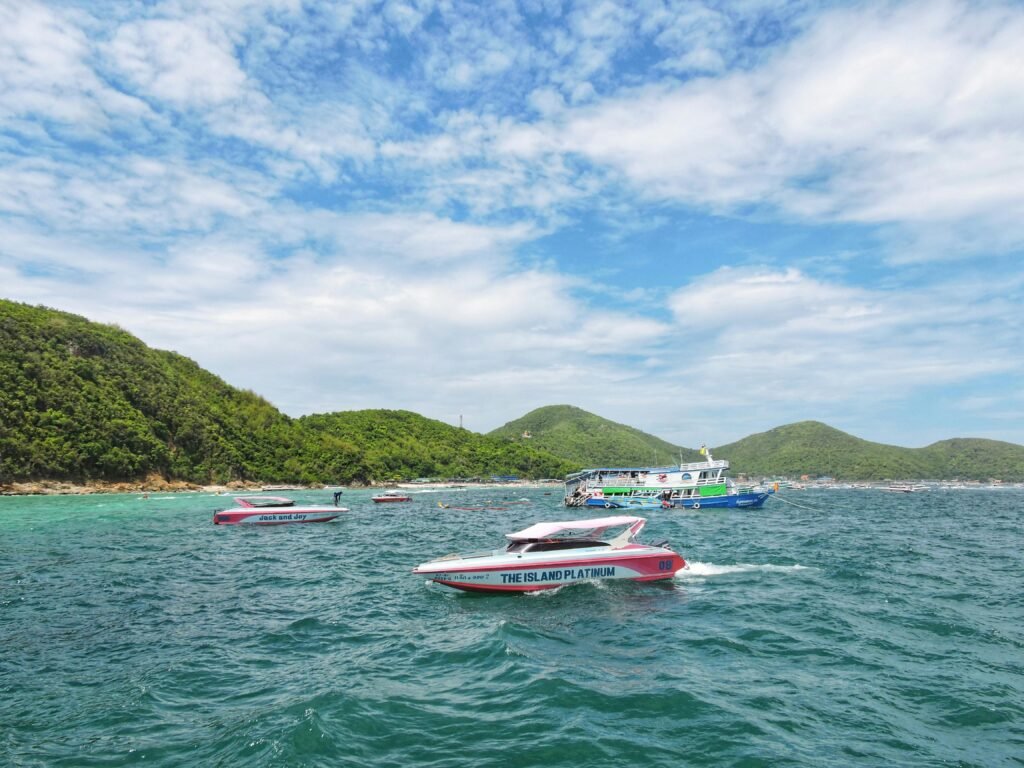 Colorful speedboats cruising near Ko Lan Island with lush hills and clear skies in Thailand.