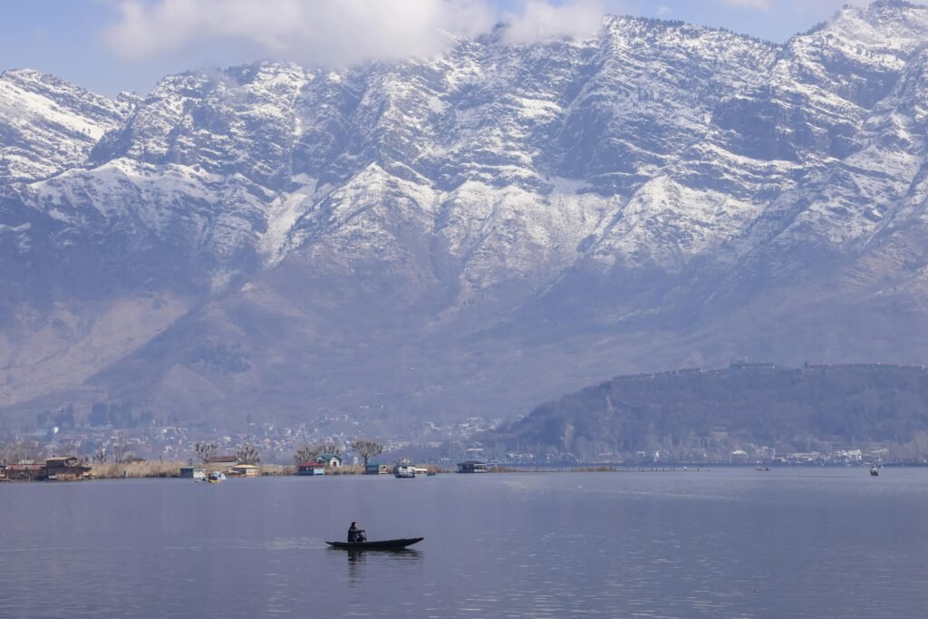 Tranquil scene of a boat on Dal Lake with snow-capped Zabarwan mountains in Srinagar.