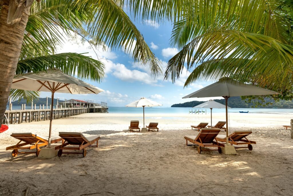 Relaxing tropical beach view with palm trees, umbrellas, and lounge chairs on a sunny day.