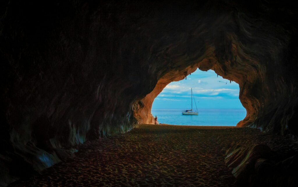 View of a sailboat from within a dark cave opening out to the bright sea.