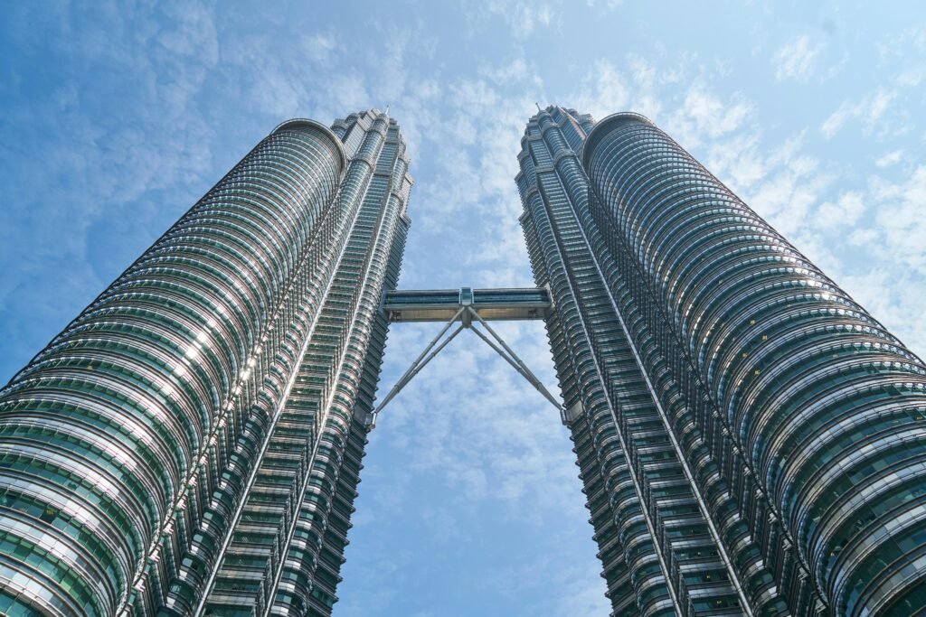 A striking low angle view of the iconic Petronas Twin Towers in Kuala Lumpur against a bright blue sky.