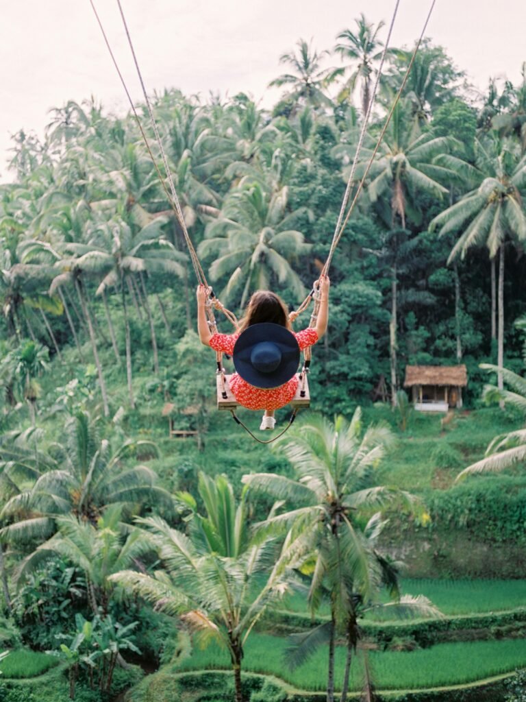 Woman enjoying a swing ride over lush tropical forest in Bali, Indonesia with palm trees surrounding.