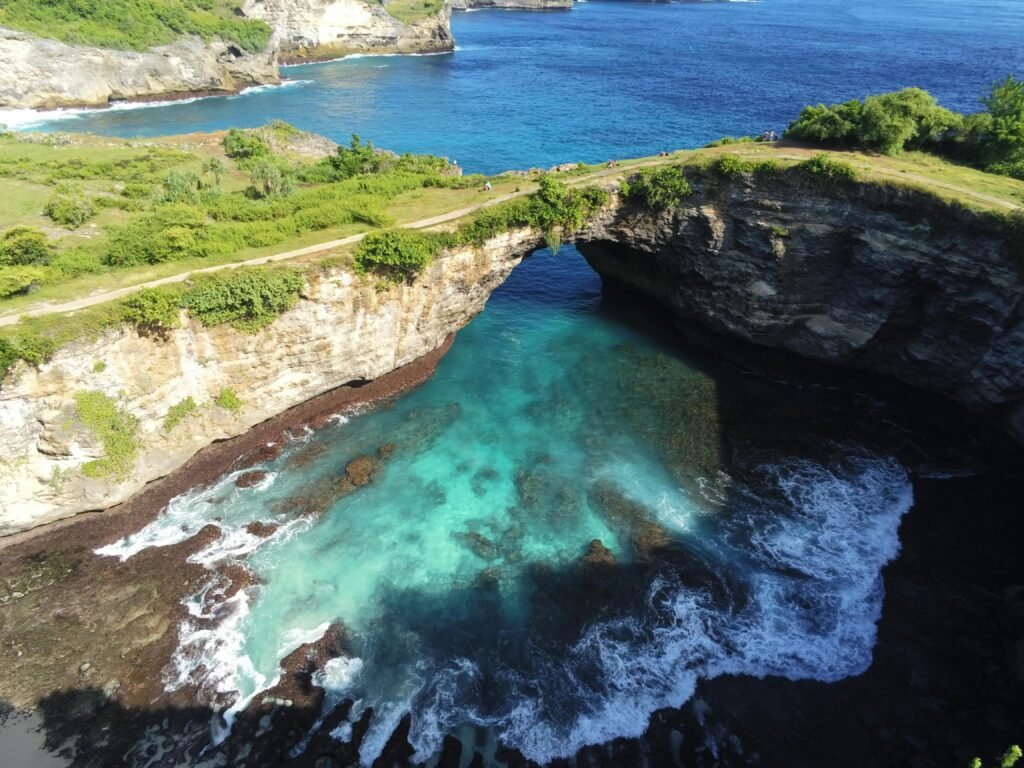 Stunning aerial view of a natural arch over turquoise waters in Bali, capturing the rugged coastline's beauty.