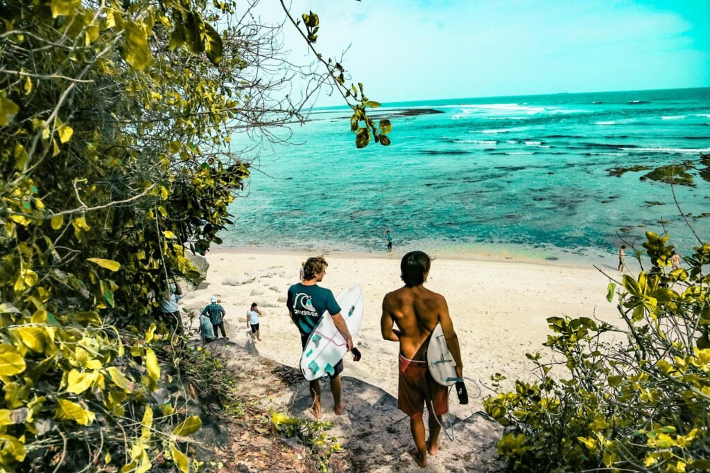 Surfers make their way down a lush path to a stunning beach in Bali, Indonesia.